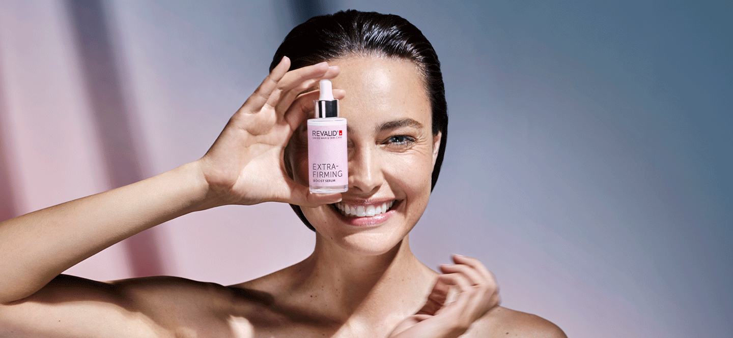 Smiling woman holding a pink skin care serum bottle in front of her face.