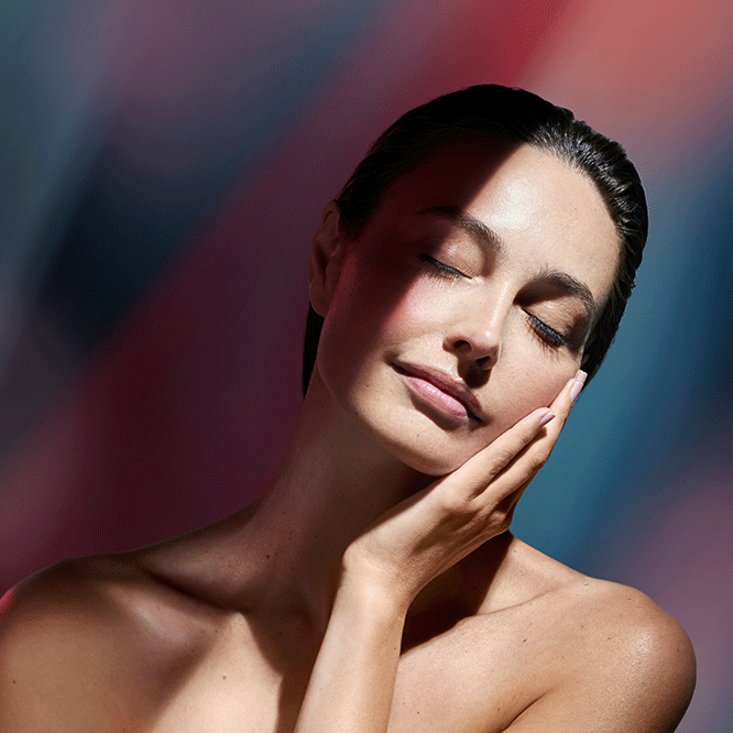 Woman with closed eyes, gently resting her hand on her cheek, bathed in soft, colored light.